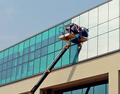Tekniker i lift monterar fönsterfilm på fönsterrutor till en kontorsbyggnad.
