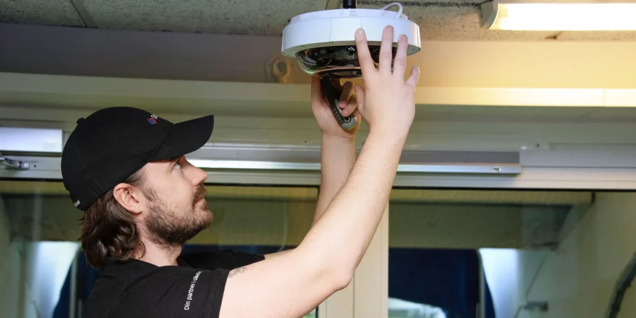 En säkerhetstekniker monterar en övervakningskamera i taket inomhus.