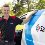 Erfaren säkerhetstekniker vid sin servicebil i bostadsområde, SafeTeams logotyp synlig på bilen.