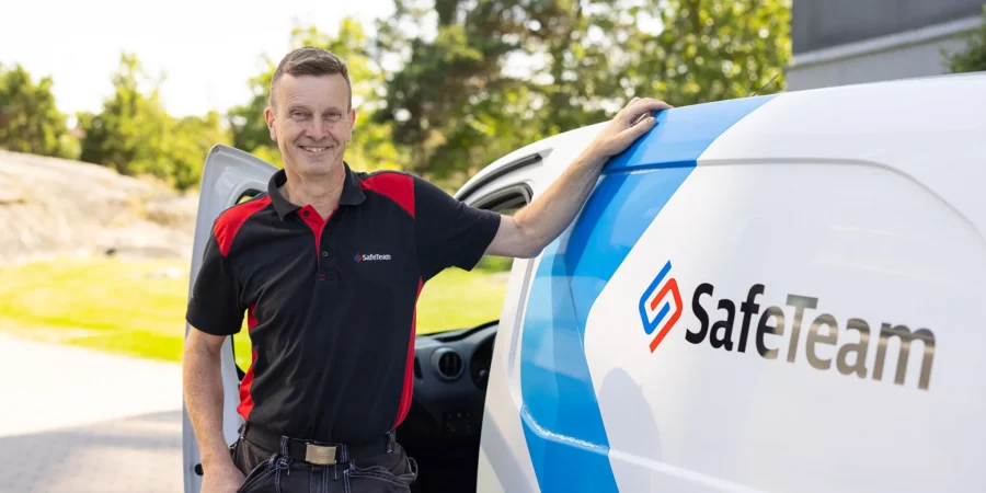 Erfaren säkerhetstekniker vid sin servicebil i bostadsområde, SafeTeams logotyp synlig på bilen.
