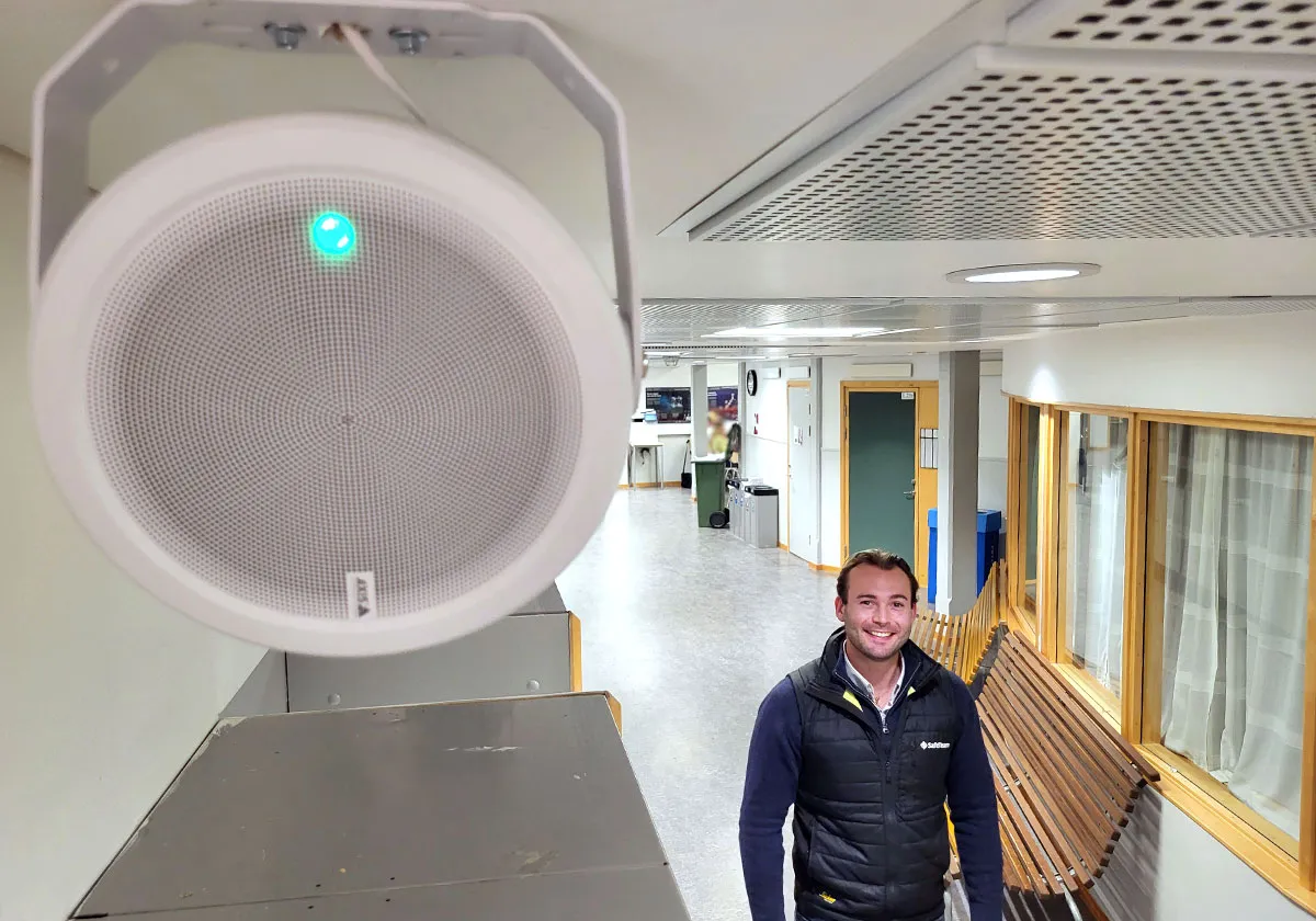 En skolkorridor där en högtalare för ett inrymningslarm sitter på väggen, i korridoren syns SafeTeams säkerhetsspecialist.