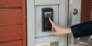 Porttelefon från Axema vid en entré, en hand bläddrar i displayen för att ringa upp någon via porttelefonen.