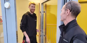 En projektör inom dörrar och säkerhet träffar en fastighetsskötare i en dörröppning i ett trapphus.