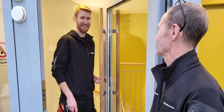 En projektör inom dörrar och säkerhet träffar en fastighetsskötare i en dörröppning i ett trapphus.